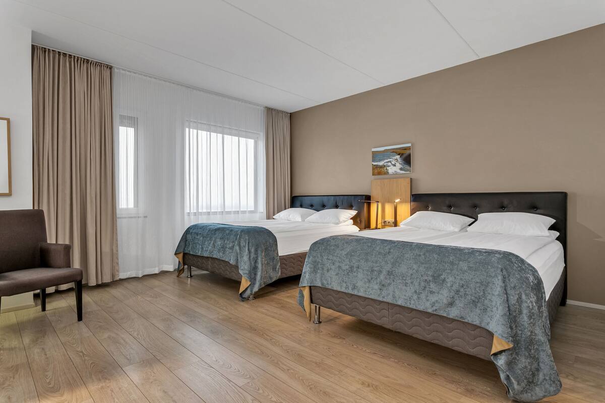 Habitación de hotel con dos camas, una silla, una lámpara y un cuadro en la pared.