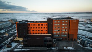 Ein mehrstöckiges Hotel mit einer markanten orangefarbenen Fassade, einem Parkplatz und einer verschneiten Landschaft im Hintergrund.