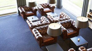 Een kamer met leren banken en fauteuils, gerangschikt rond een centrale salontafel, met lampen aan weerszijden.
