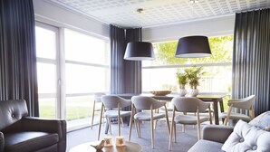 Een moderne woonkamer met een bank, stoelen, een eettafel en een groot raam met gordijnen.