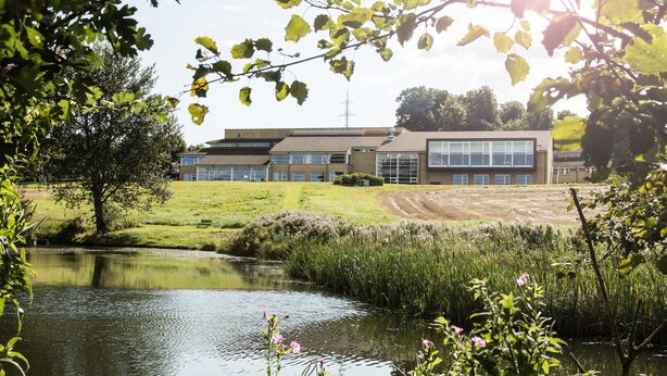 Een gebouw in moderne architectuur, omgeven door grasvelden en een waterpartij.