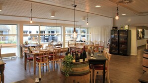 Een ruim restaurant met houten meubels, grote ramen en een wijnrekken.
