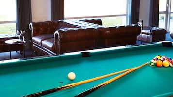 A pool table with balls and cues, a leather sofa, and a small table with glasses.