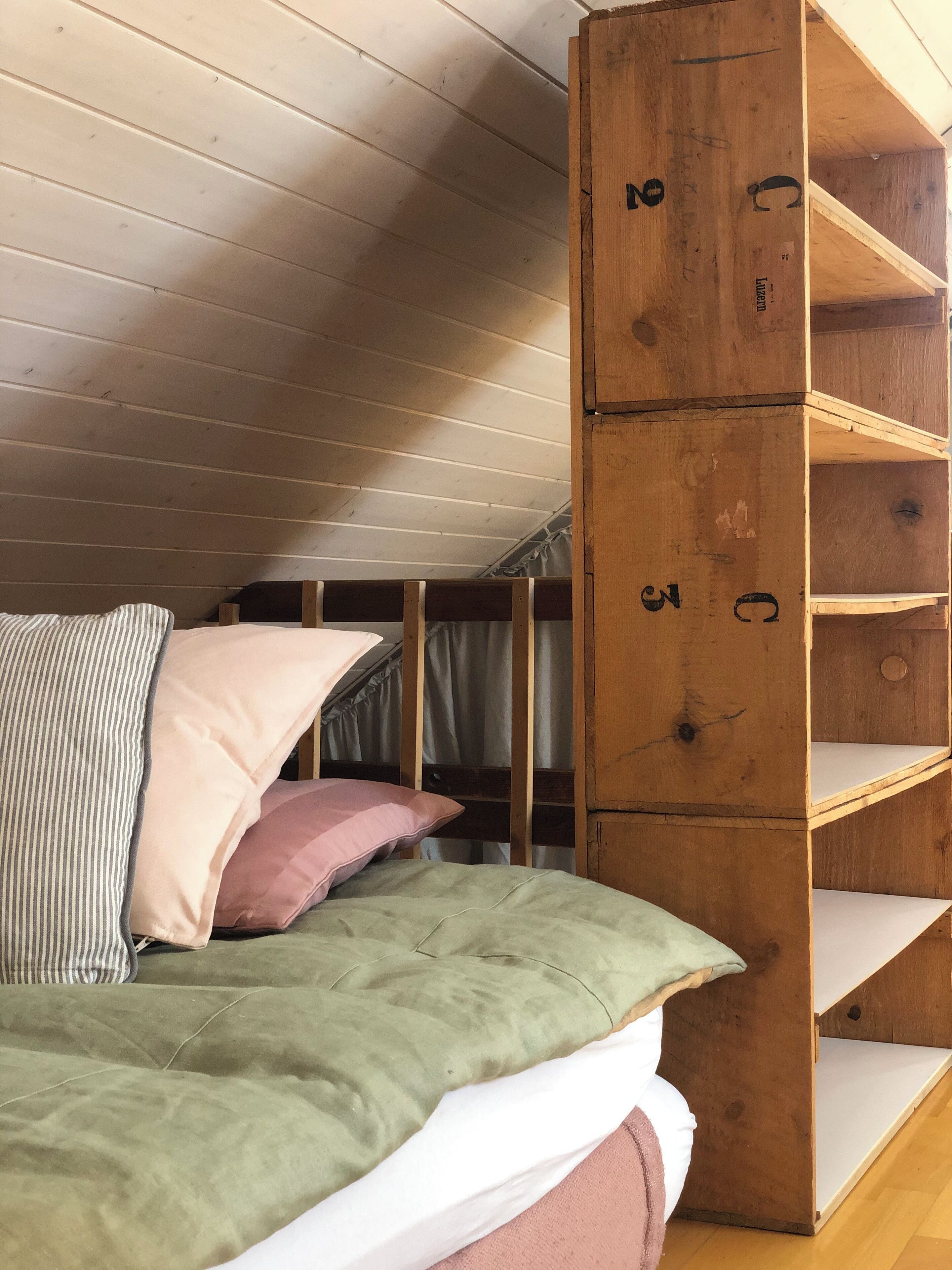 A bunk bed with a green mattress and pillows, a wooden bookshelf, and a slanted ceiling.
