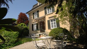 A two-story building with a garden patio featuring outdoor seating. - The Bed and Breakfast (Lucerne)