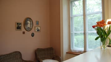 A room with two wicker chairs, a white table, and a window with a view of trees.