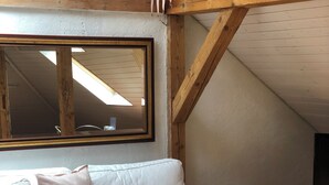 A cozy attic room with a white sofa, a wooden coffee table, and a large mirror. - The Bed and Breakfast (Lucerne)