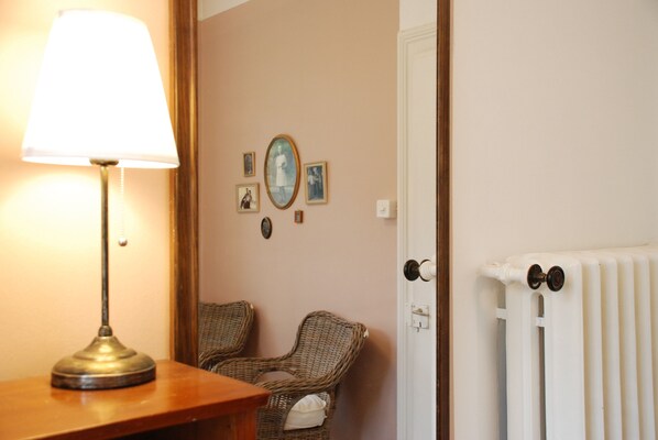 A room with a lamp, wicker chairs, a radiator, and framed pictures on the wall.