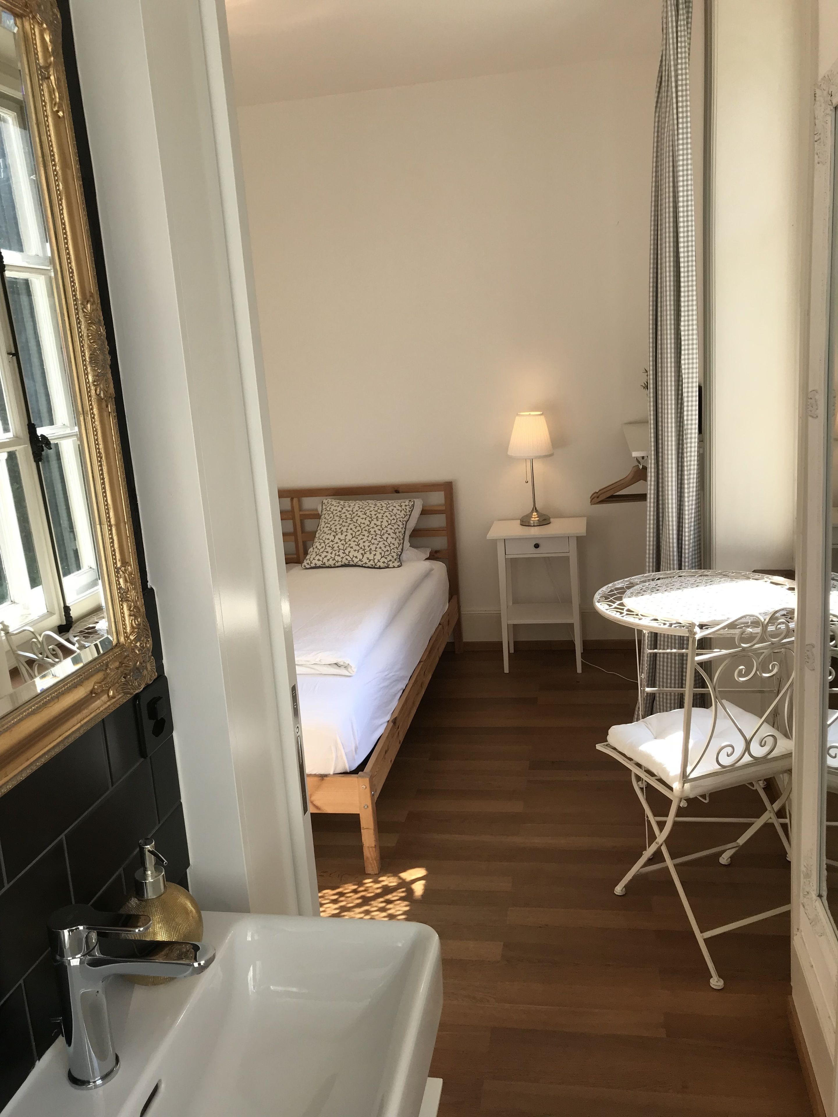 A bedroom with a bed, bedside table, lamp, and a small round table with a chair.