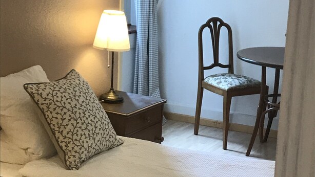 A bedroom with a bed, a nightstand, a lamp, a chair, and a table. - The Bed and Breakfast (Lucerne)