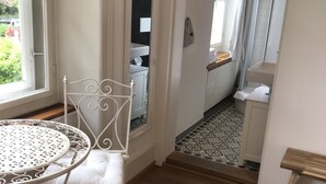 A bedroom with a bed, a small table with a chair, a window, and a bathroom visible through an open door. - The Bed and Breakfast (Lucerne)