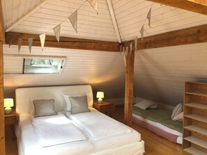 A cozy bedroom with a large bed, a smaller bed, wooden beams, a window, and a wooden shelf. - The Bed and Breakfast (Lucerne)
