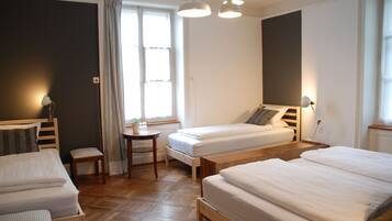 Ein Zimmer mit zwei Einzelbetten, einem kleinen Tisch, einem Stuhl und einem Fenster mit Vorhängen.