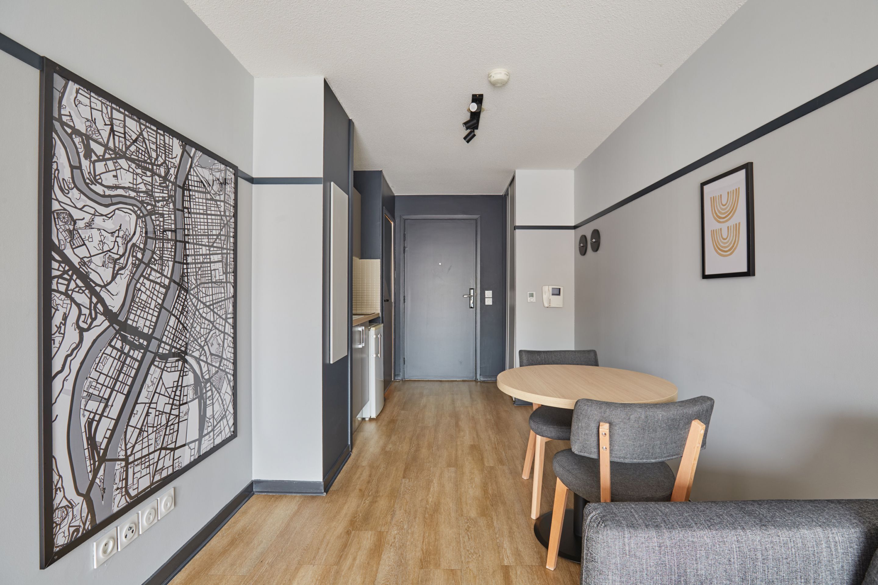 Una habitación de hotel moderna con suelo de madera, un área de comedor con una mesa redonda y sillas, una gran obra de arte abstracto en la pared y una puerta que da a otra habitación.