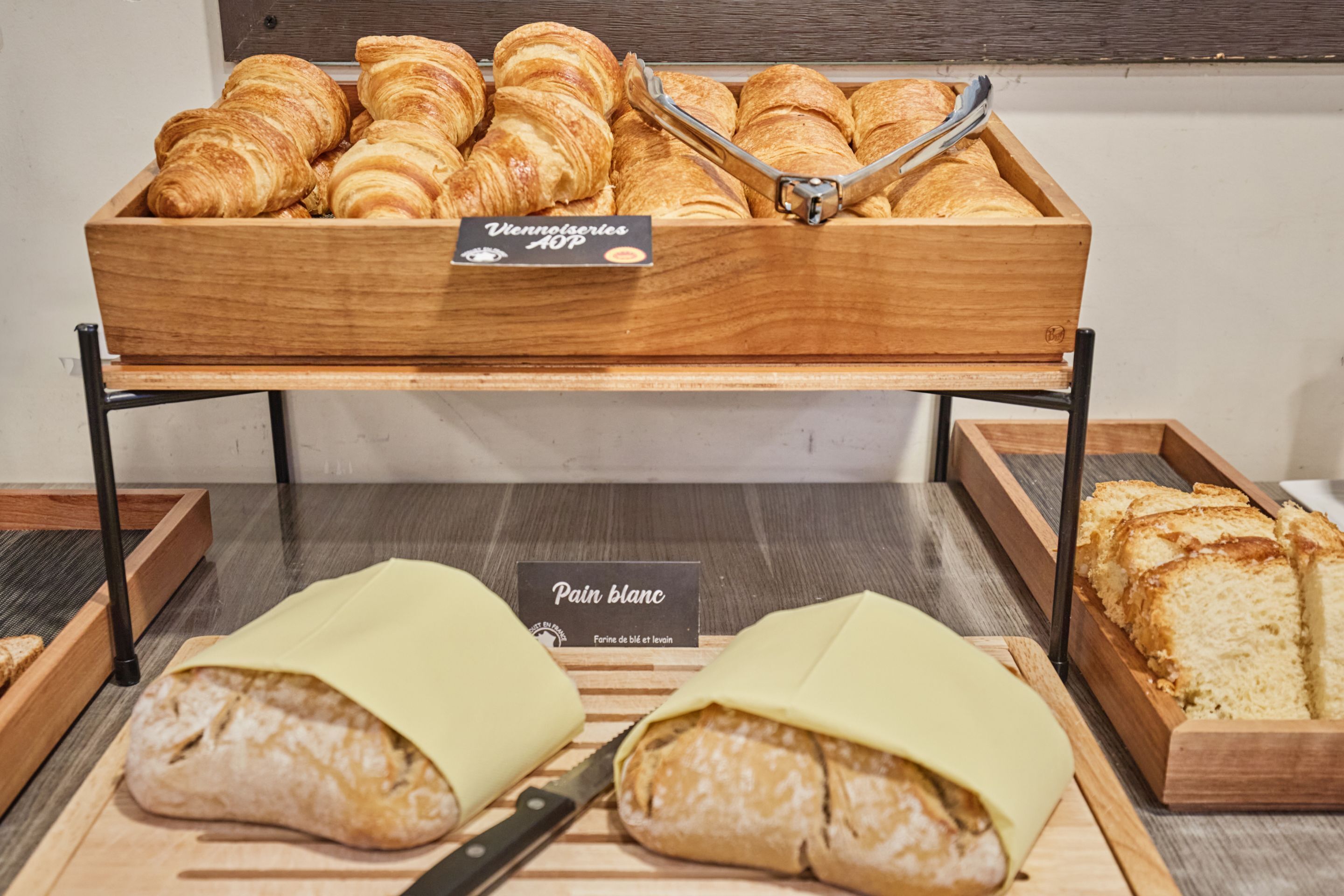 Une vitrine de boulangerie présentant des croissants et du pain, avec les étiquettes « Vennelseries » et « Pain blanc ».