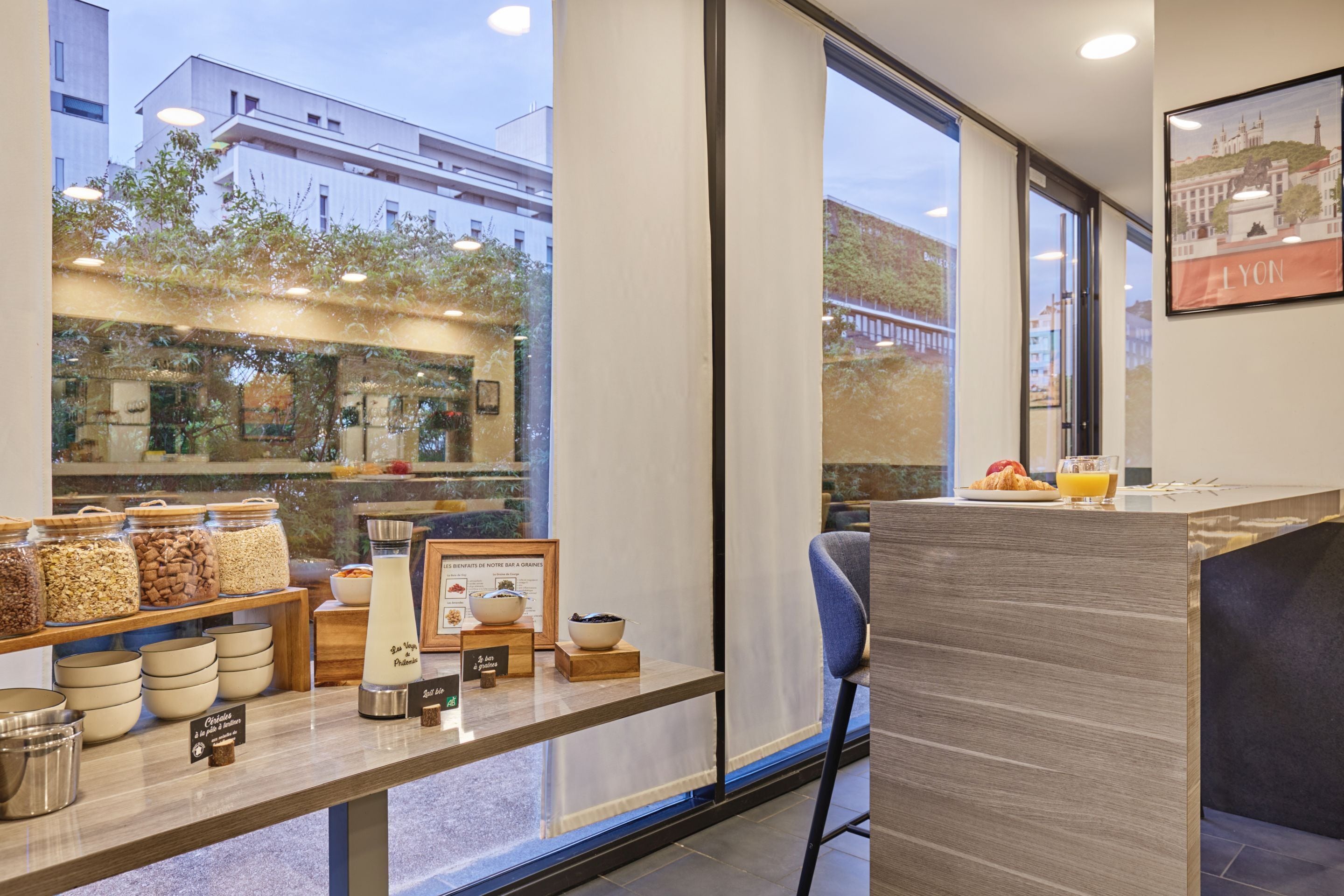 A modern café with a wooden counter, various food items, and a view of the city.