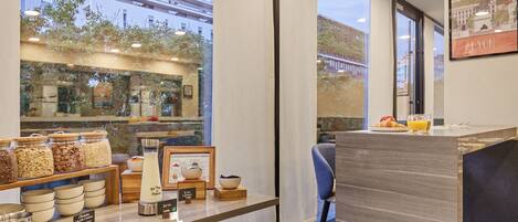 A modern café with a wooden counter, various food items, and a view of the city.
