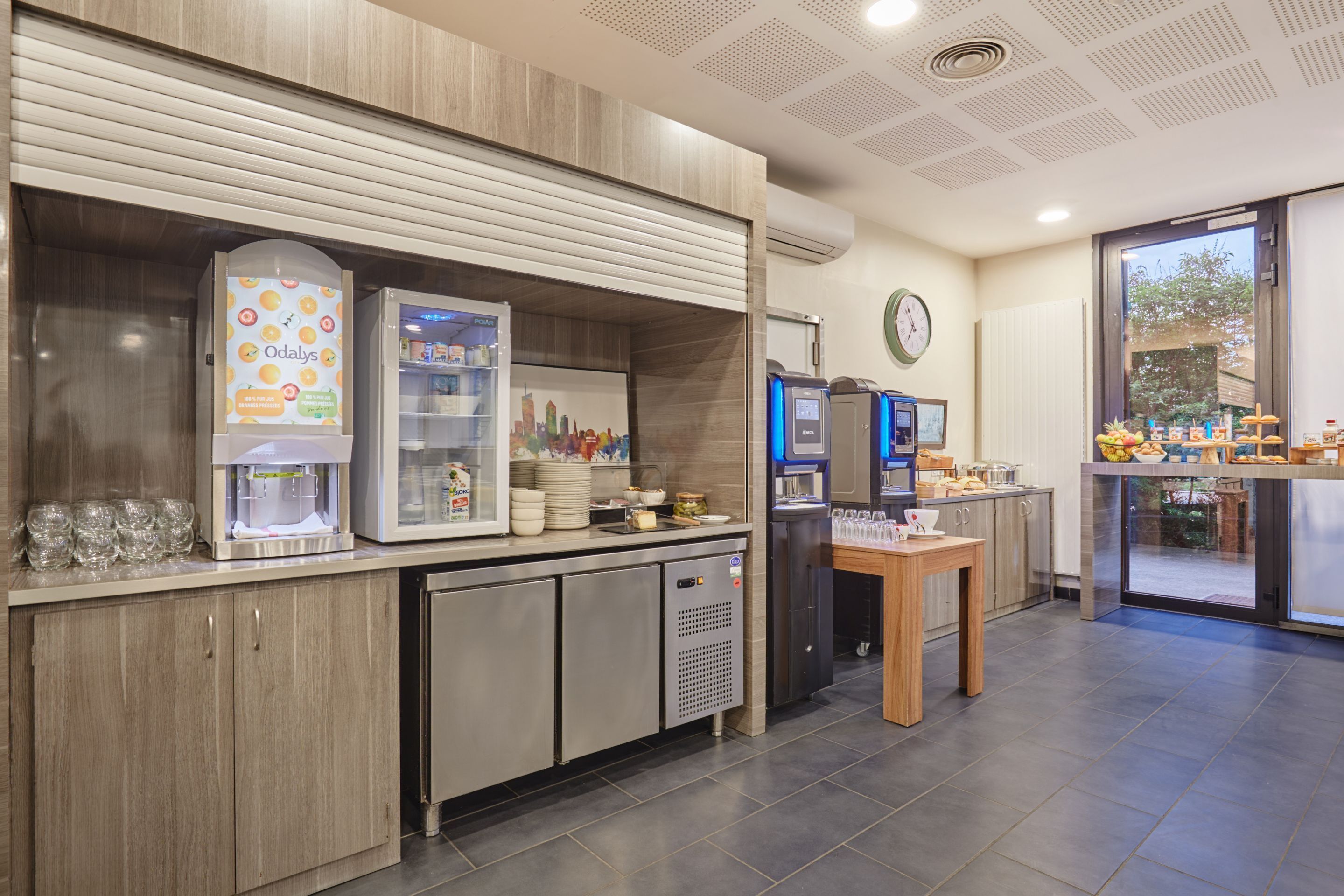 A modern kitchen area with a coffee machine, a refrigerator, and a small table with a cup and saucer.
