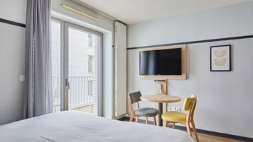 Una camera d'albergo con un letto, una TV fissata al muro, un tavolino rotondo con due sedie e un balcone con vista.