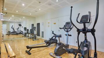 A gym with various exercise machines, a wooden floor, and a large mirror.
