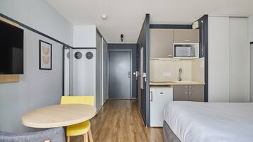 Een compacte hotelkamer met een bed, een kleine kitchenette, een zithoek met een tafel en stoelen, en een deur naar een andere kamer.