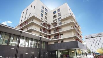 A modern multi-story building with balconies, large windows, and a flat roof.