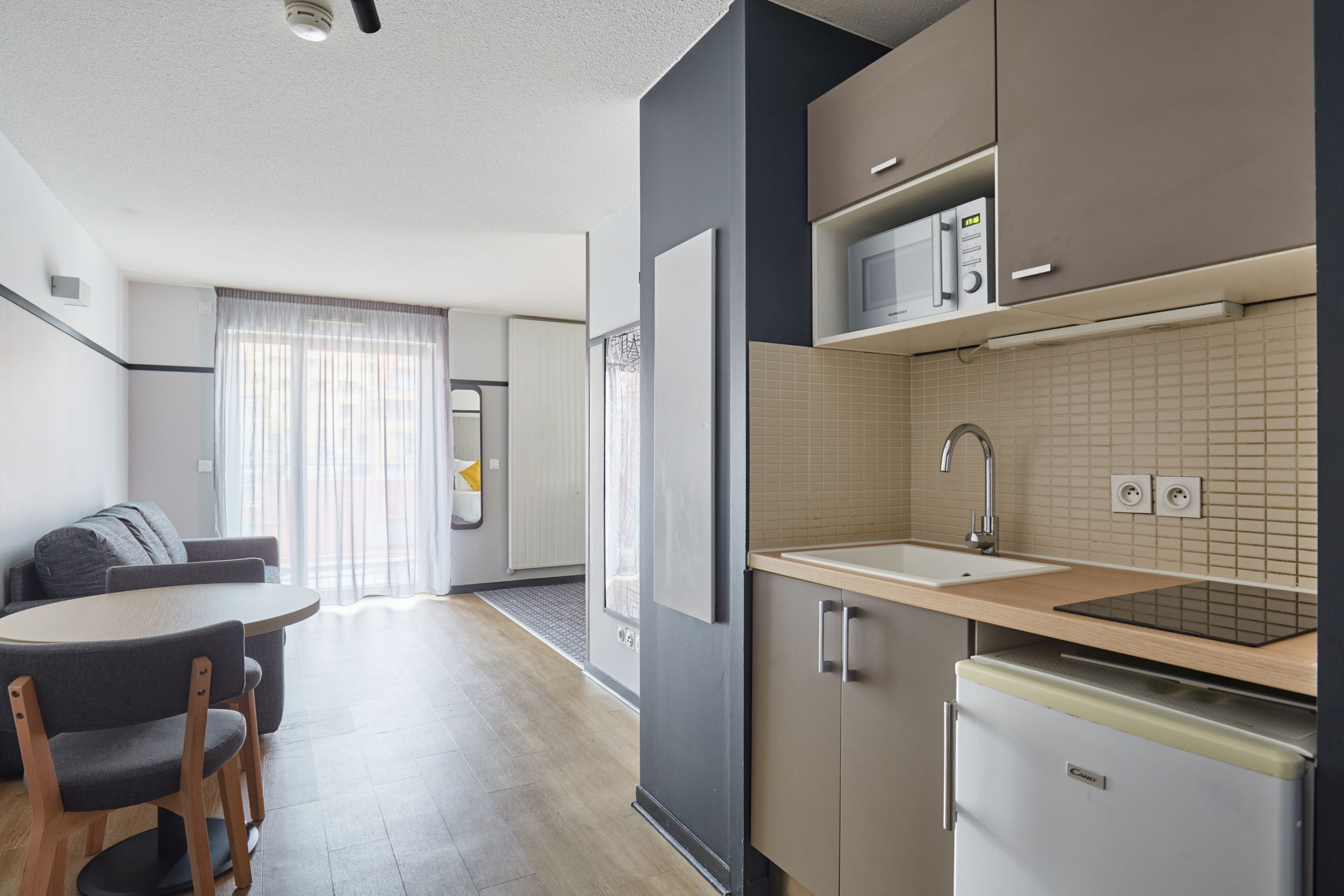 A modern kitchen with a microwave, sink, and refrigerator. There is a dining area with a table and chairs.