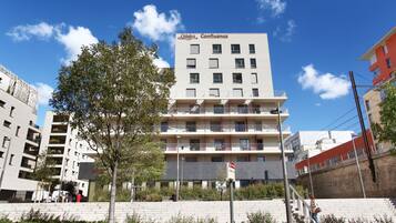 A multi-story hotel with balconies, a clear sky, and a brick wall in the foreground.