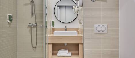 Ein modernes Badezimmer mit einer Duschkabine, einem Waschbecken mit Spiegel darüber, einem Fön und einer Toilette.