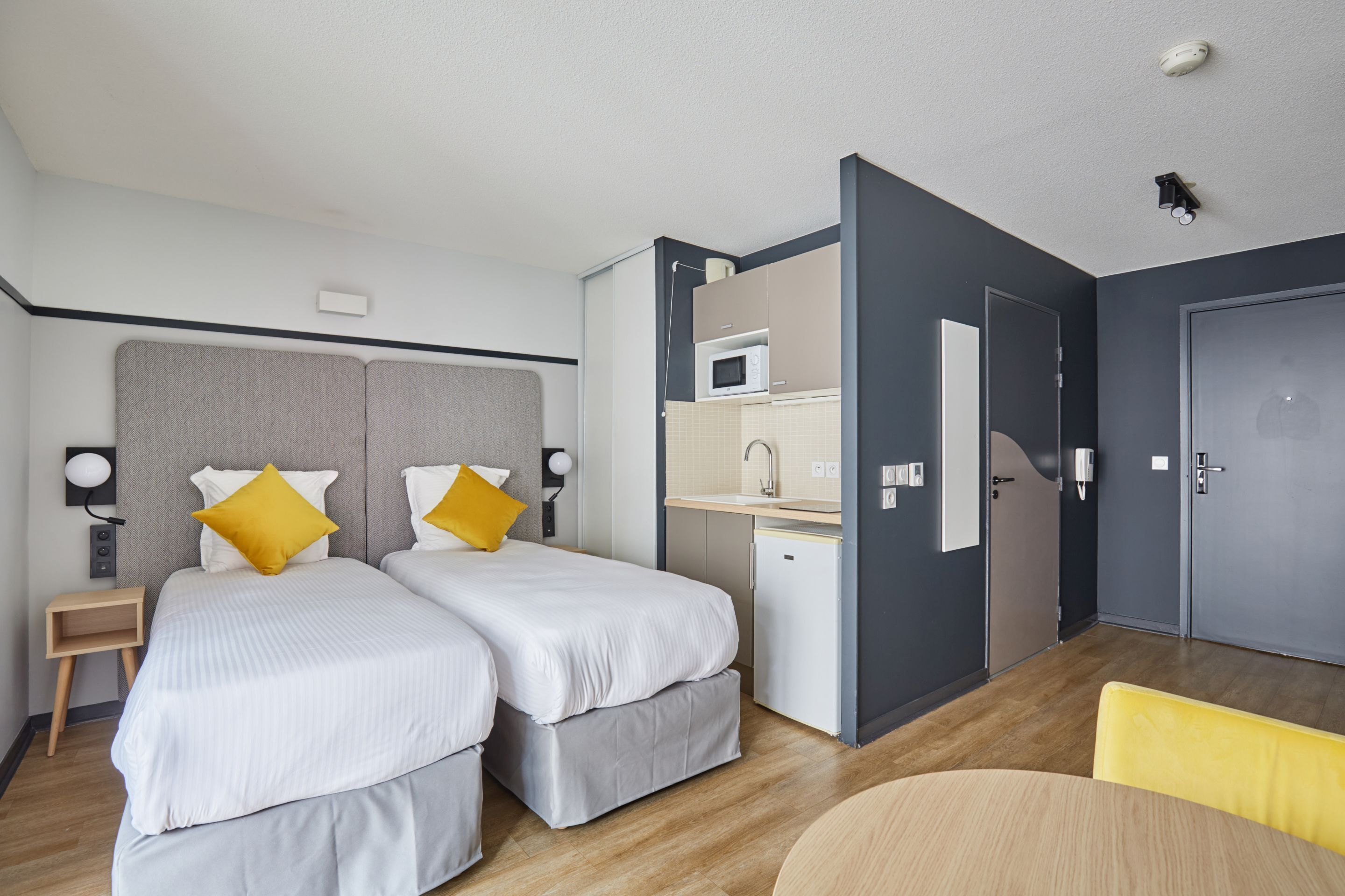 Habitació d'hotel amb dos llits, una taula de treball, microones i una porta.