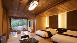 A hotel room with two beds, a dining area, and a view of a forest.