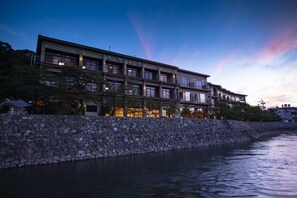 Un hotel de varios pisos con un muro de piedra y un río en primer plano.