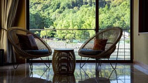 A room with two wicker chairs facing a large window overlooking a forested area.