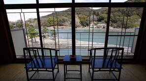Una habitación con dos sillas frente a un amplio ventanal con vistas a un cuerpo de agua y colinas.