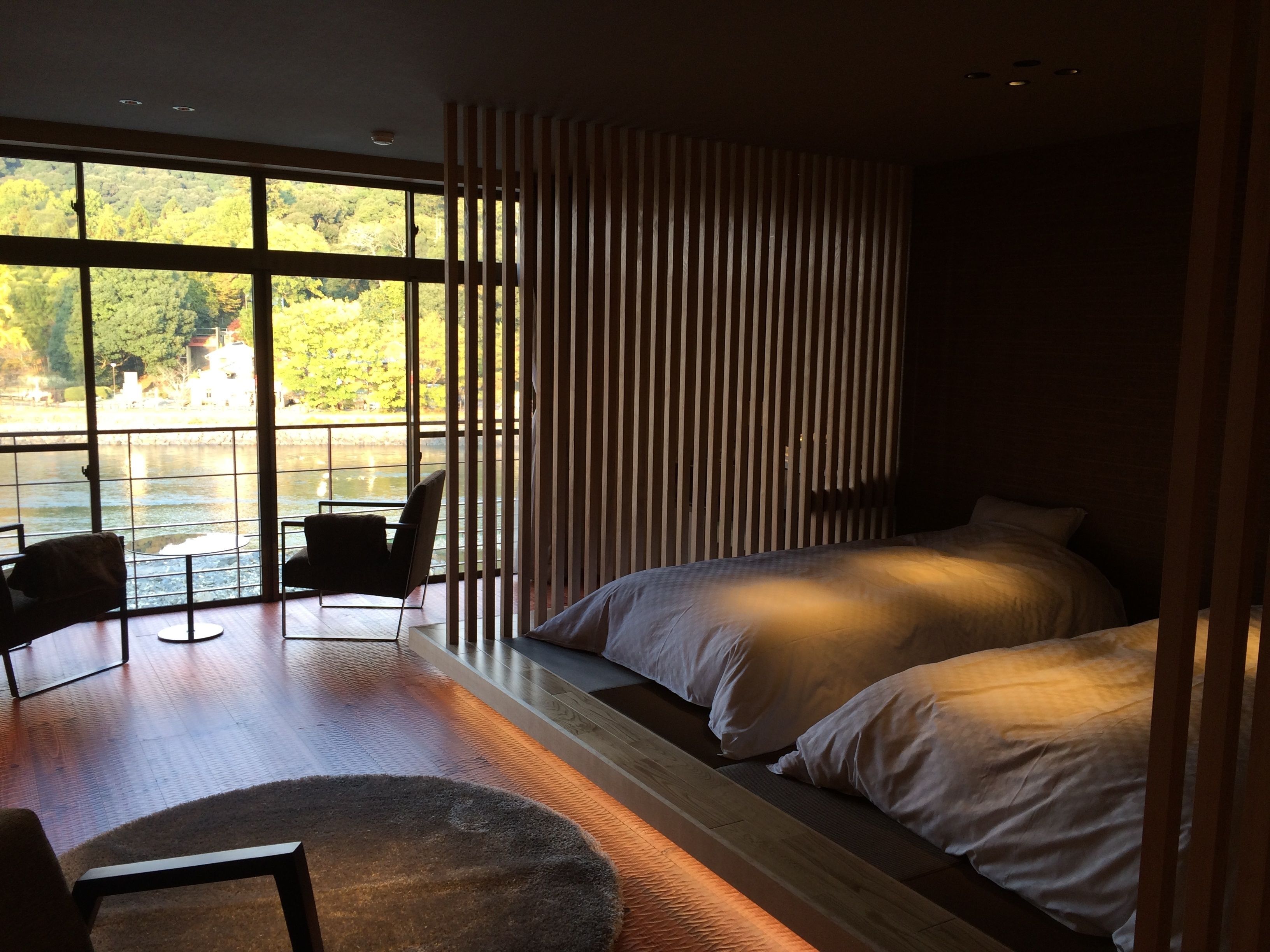 A modern bedroom with a large window, a bed, a chair, and a small table.