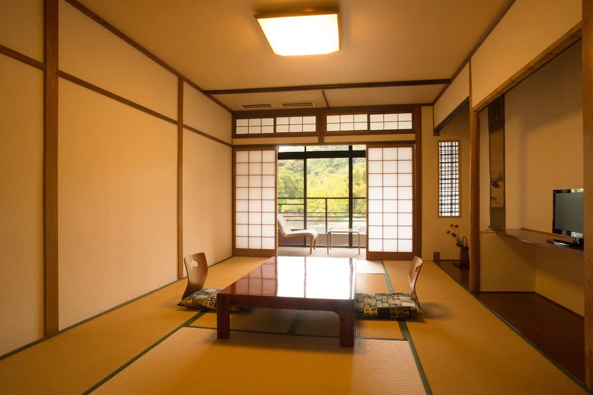 A traditional Japanese room with tatami flooring, a low wooden table, and sliding doors leading to a balcony with a view of greenery.