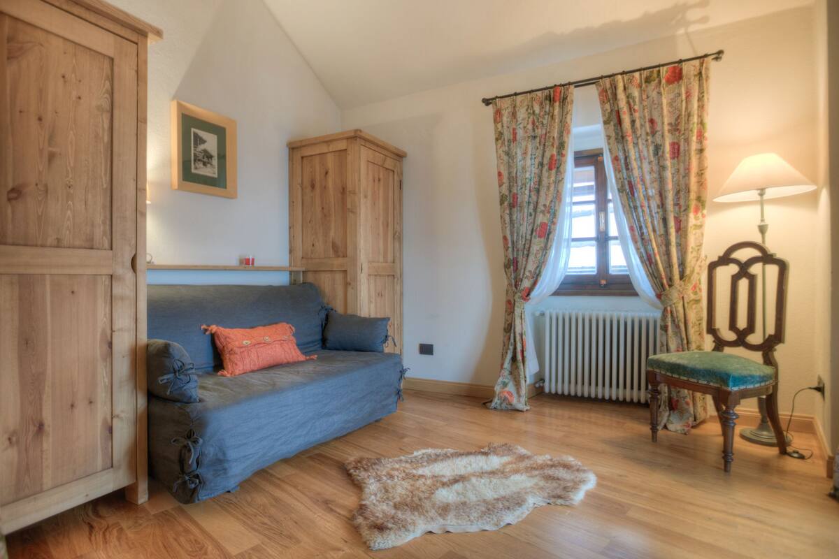 Una habitación acogedora con un armario de madera, un sofá azul, una cortina estampada y un radiador, además de una lámpara.