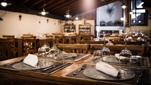 Interior de restaurante con mesas de madera dispuestas para comer, con cristalería y cubertería visible.