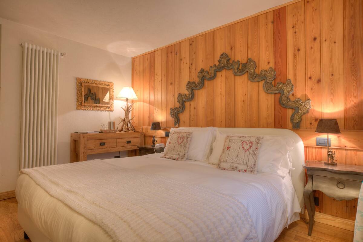 Un dormitorio con cabecera de madera, una cama con ropa blanca, un aparador de madera y una mesita de noche con lámpara.