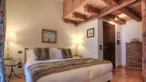 Un dormitorio con una cama grande, vigas de madera en el techo, un aparador y dos lámparas de pared.