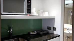 A modern kitchen with a built-in microwave, a stainless steel sink, and a green backsplash. - Arch hotel (London)