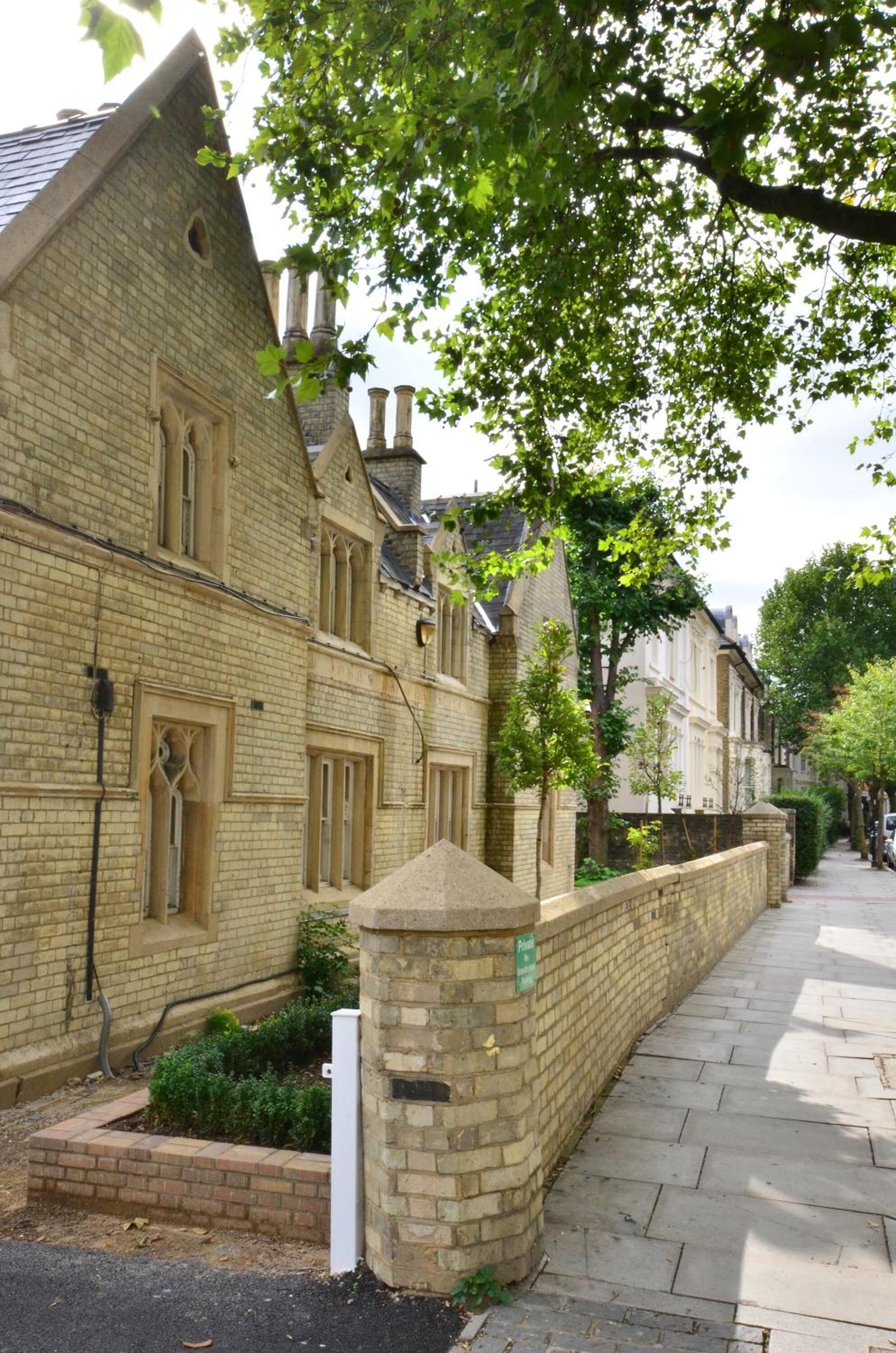A row of traditional brick buildings with uniform windows and a stone wall separating the sidewalk from the road.