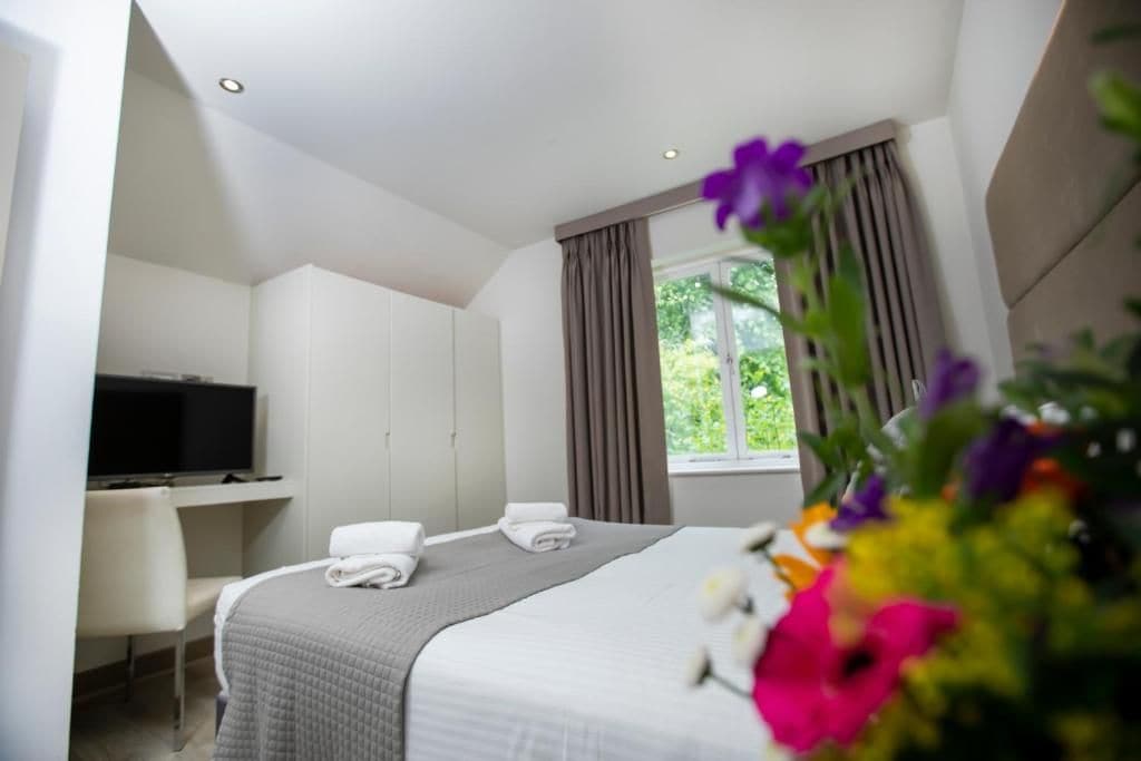 Ein Hotelzimmer mit einem Bett, einem Schreibtisch mit Fernseher und einem fenster mit Vorhängen.