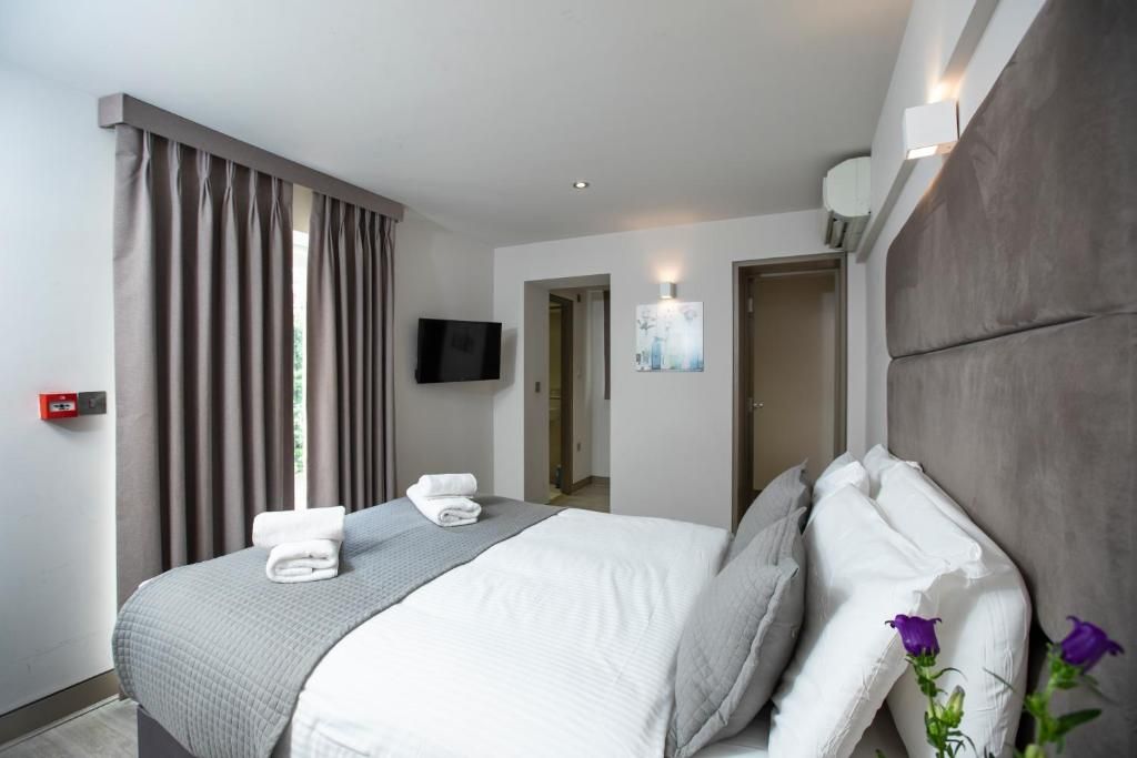A hotel room with a bed, curtains, a flat-screen TV, and a painting on the wall.