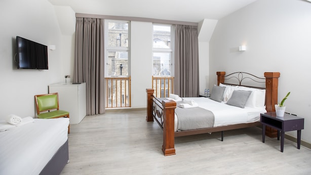 A hotel room with a bed, a TV, a desk, a chair, and a window with curtains. - Arch hotel (London)