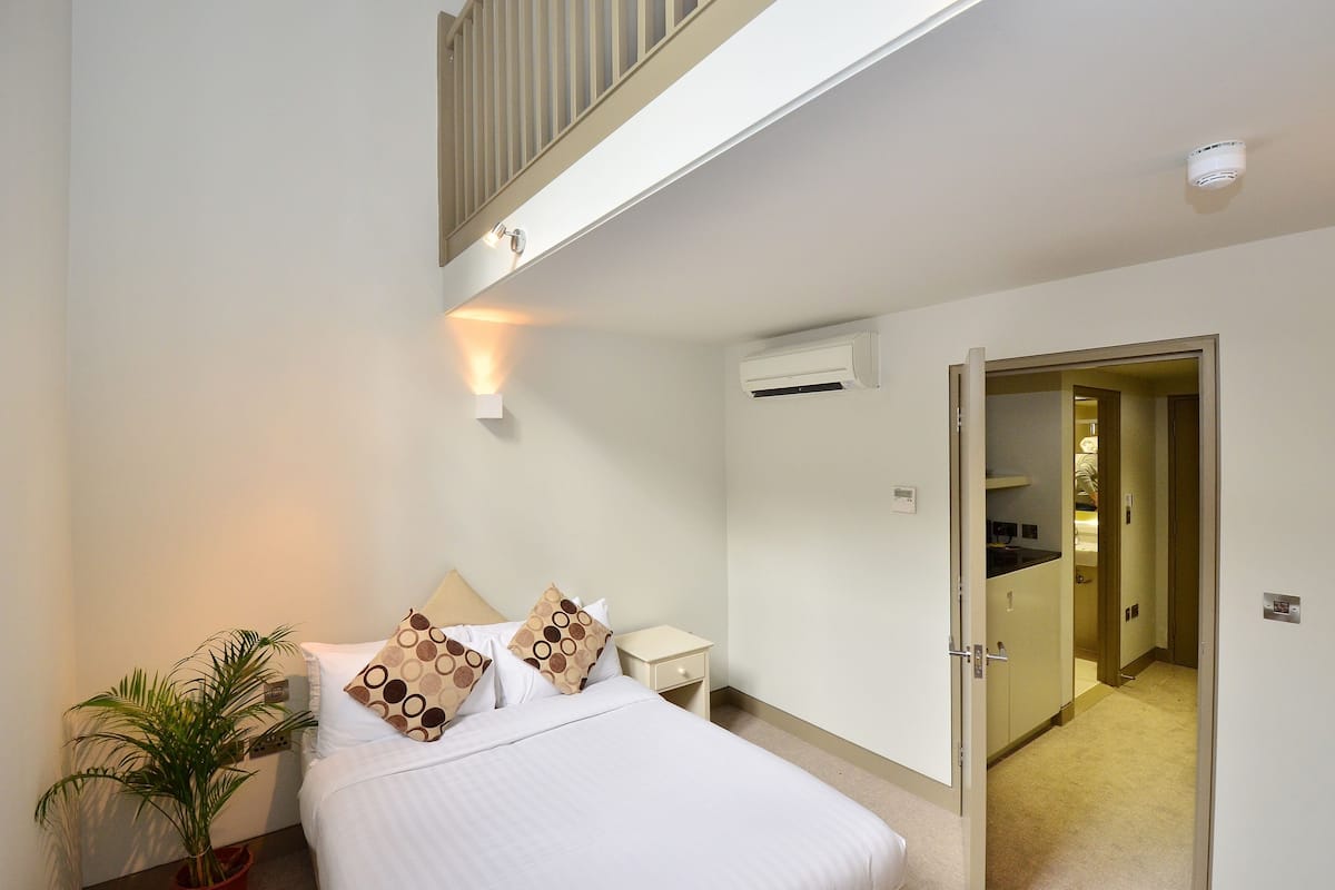 Ein Schlafzimmer mit Bett, Nachttisch, Topfpflanze und Klimaanlage.