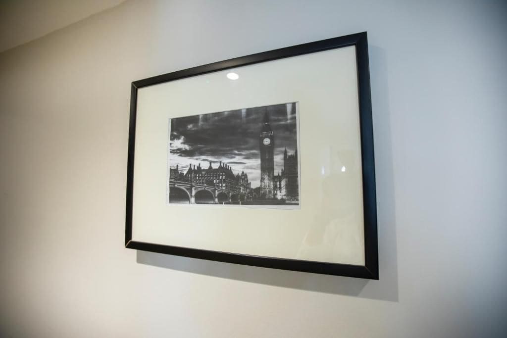 A framed black and white photograph of a cityscape with a prominent clock tower, mounted on a plain wall.