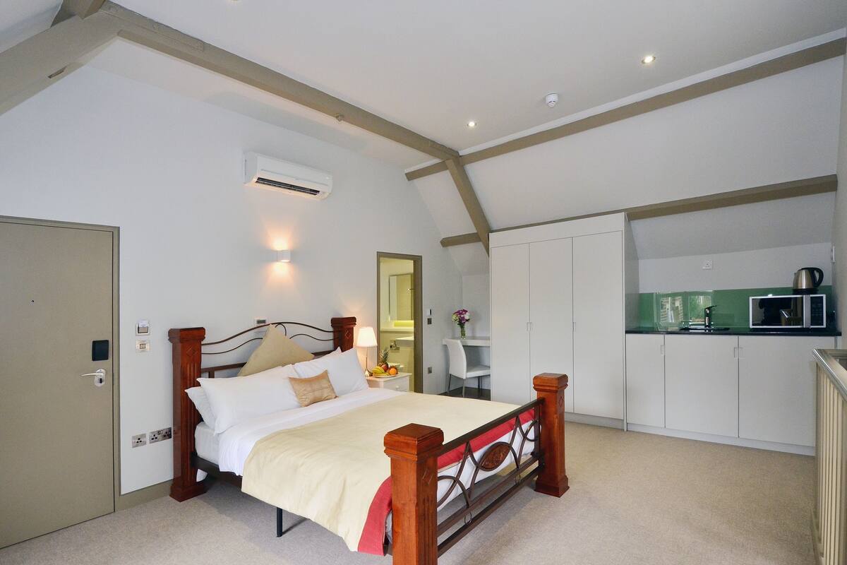 Ein Schlafzimmer mit einem hölzernen Bett, einem kleinen Schreibtisch und einer Küchenzeile.