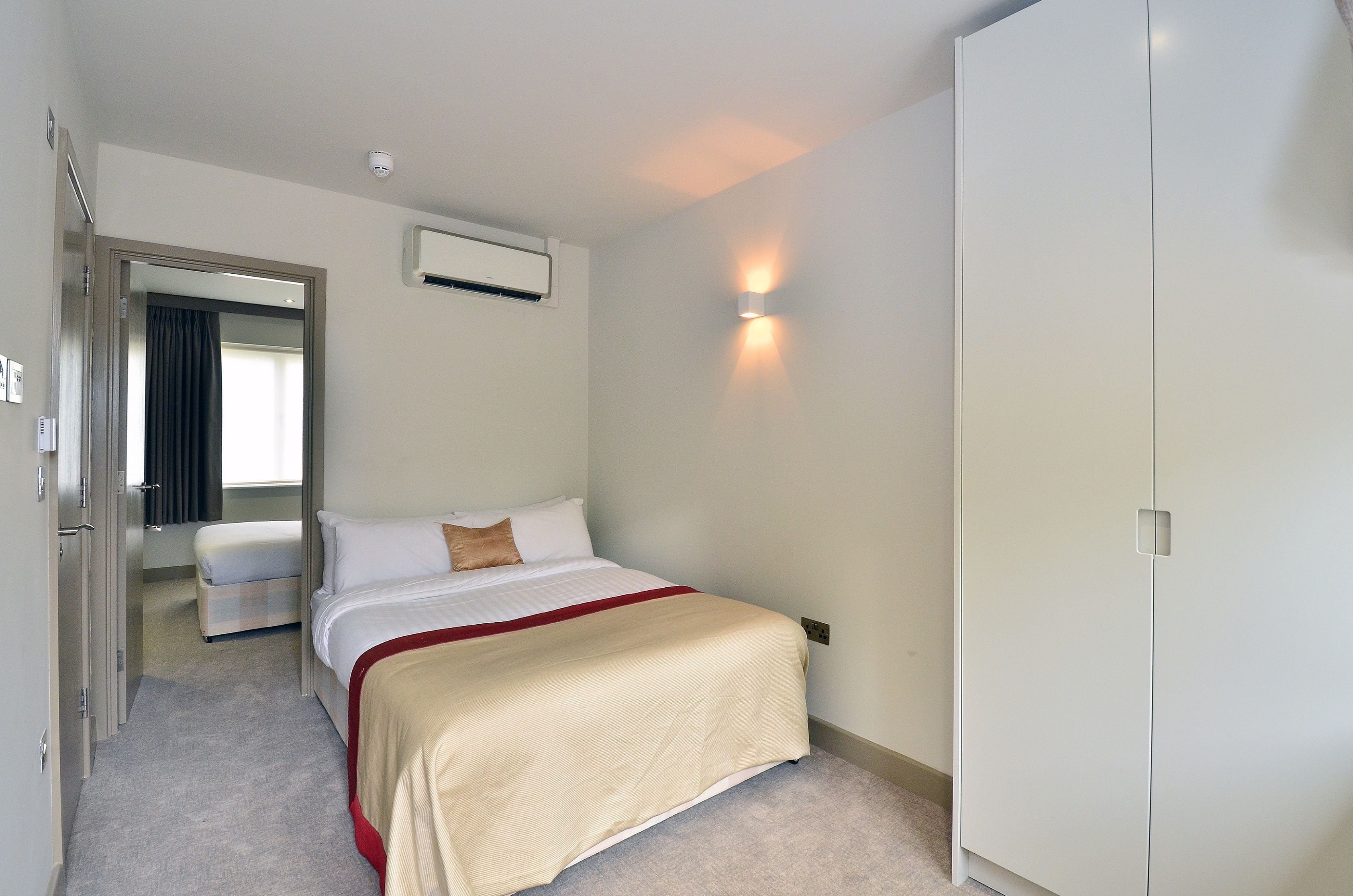 Hotellihuone, jossa on sänky, yöpöytä, ilmastointilaite ja vaatekaappi.