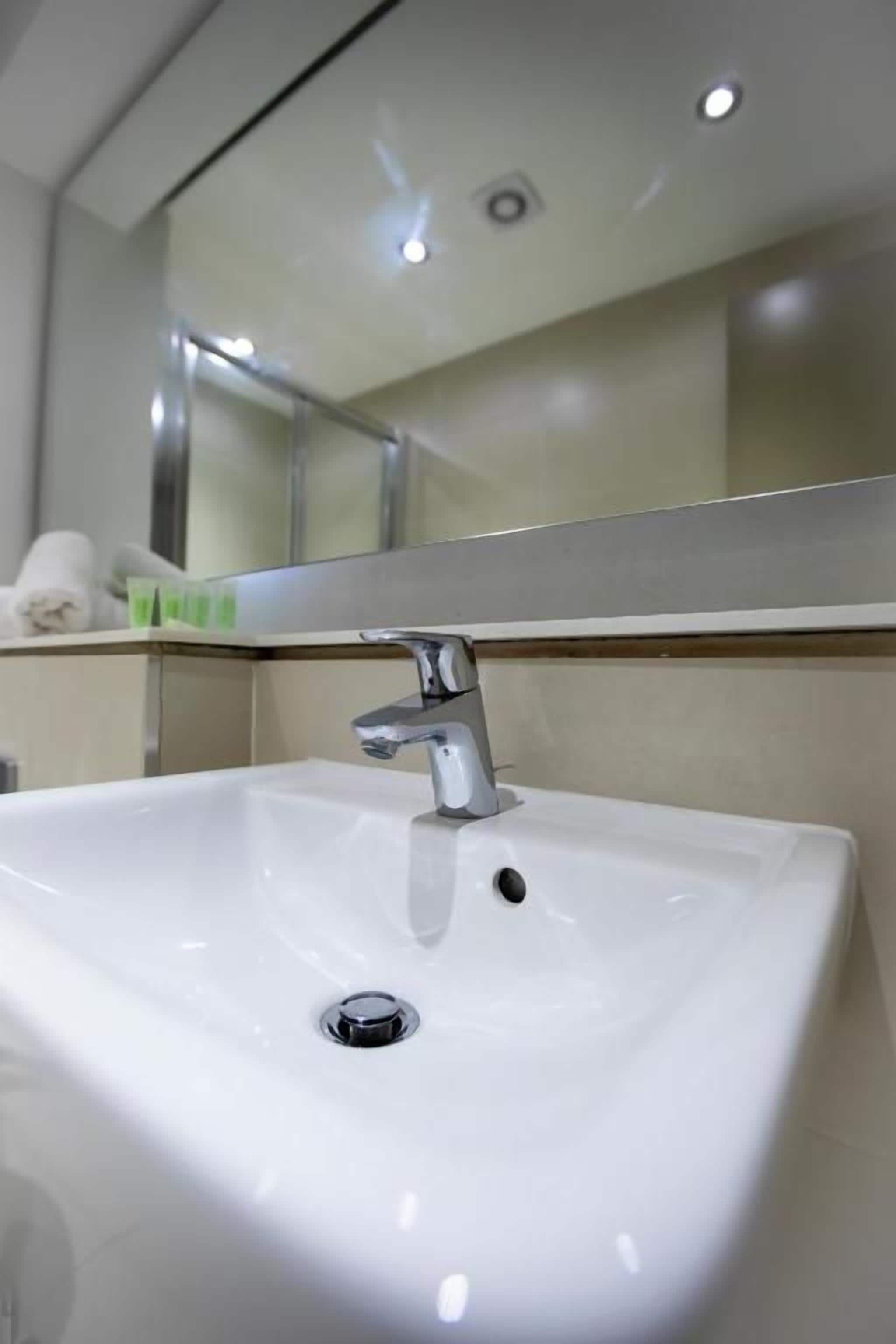 A white bathroom sink with a chrome faucet, a mirror above it, and a light fixture on the ceiling.